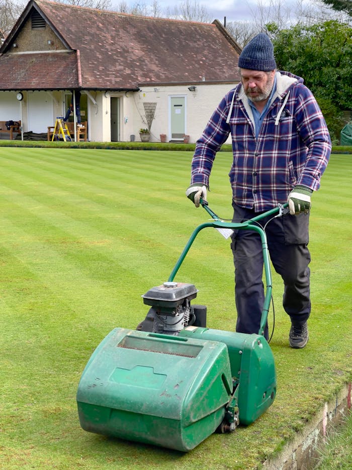A man using a lawnmower to cut grass in a garden setting in Greater London.
