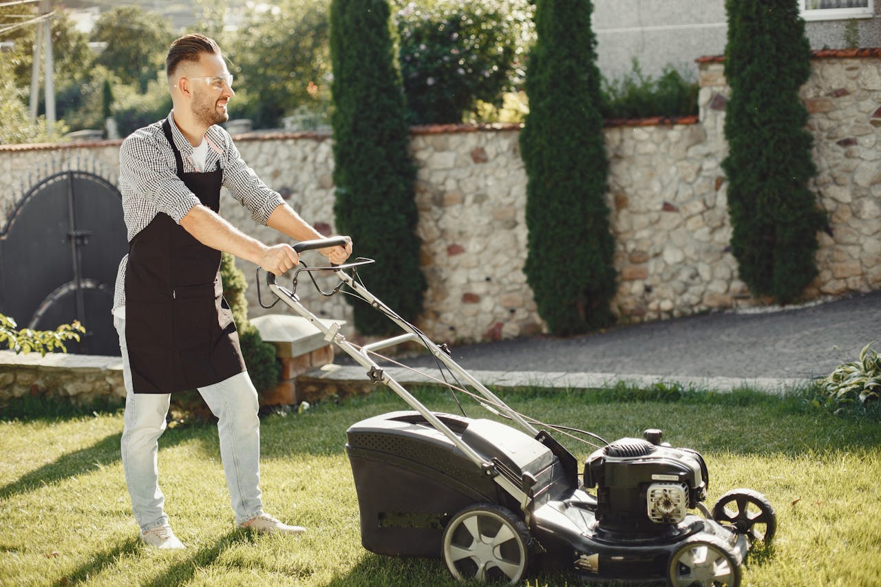 A man using a lawn mower to trim grass in a sunny outdoor garden.